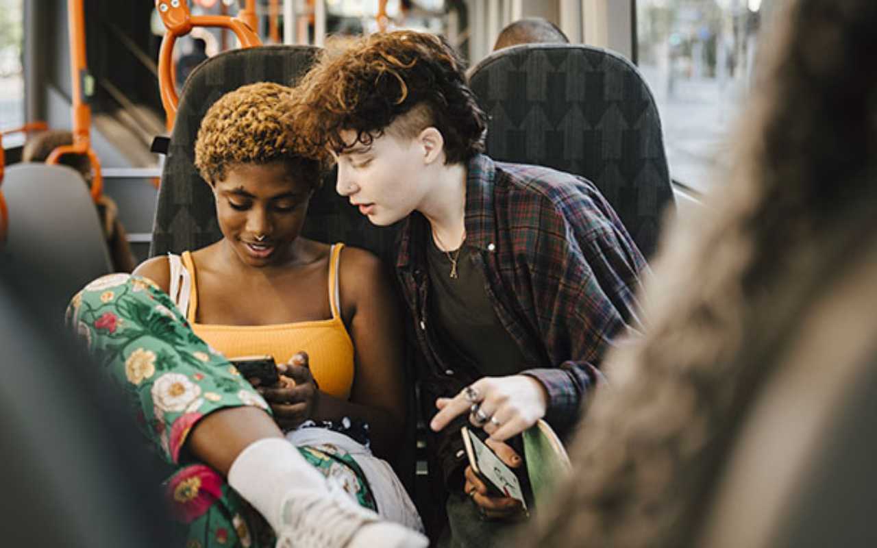 Two teens using their phones on public transportation